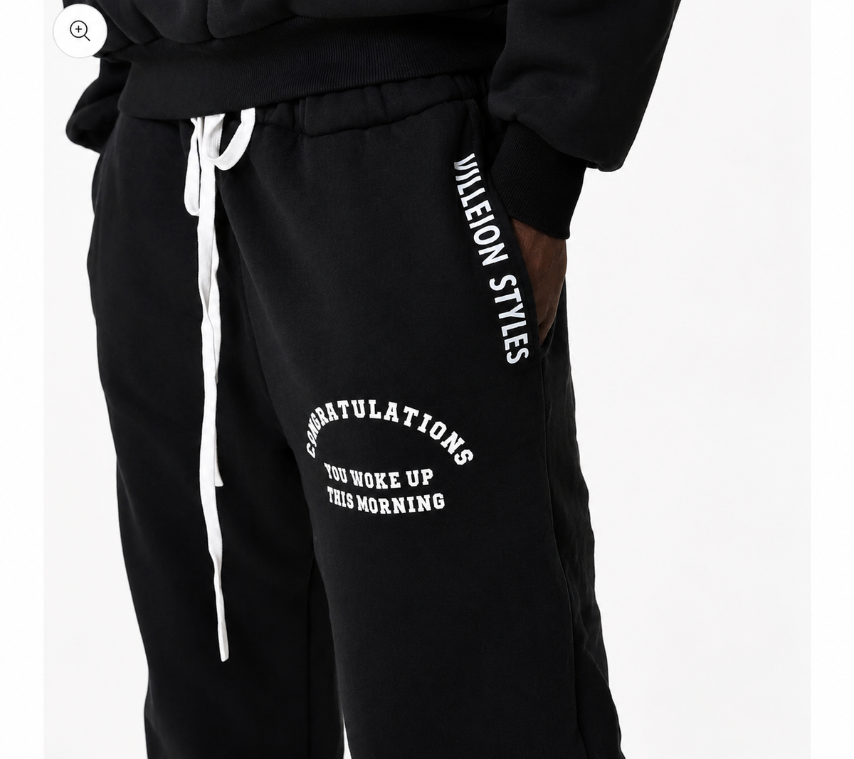 Black sweatpants with white drawstrings and white printed text on the left leg reading 'CONGRATULATIONS YOU WOKE UP THIS MORNING' and 'JULEION STYLES' printed vertically on the right leg.