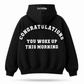 A black pullover hoodie shown from the back, featuring the phrase 'CONGRATULATIONS YOU WOKE UP THIS MORNING' printed in large white arched letters, with '1 in 4 trillion' printed in small white text inside the back collar.