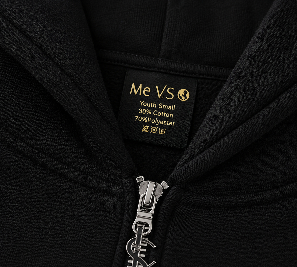 Close-up of a black zip-up hoodie showing the inner neck label with 'Me VS' and 'Youth Small 30% Cotton 70%Polyester' in gold text, plus a silver zipper with a matching metal pull.