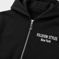 Close-up of a black zip-up hoodie with a silver zipper and white text reading 'VILLEION STYLES New York' on the chest.