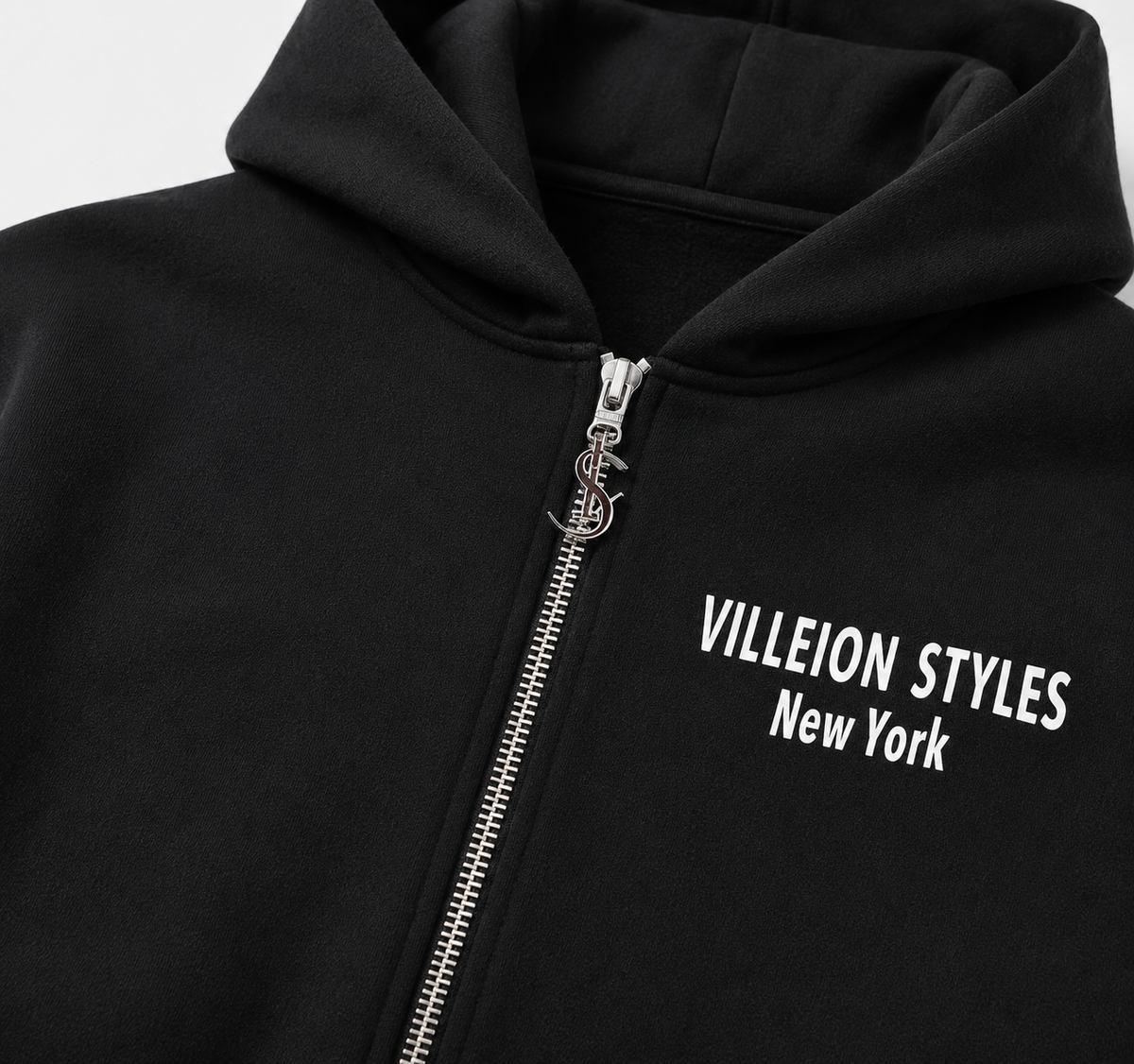 Close-up of a black zip-up hoodie with a silver zipper and white text reading 'VILLEION STYLES New York' on the chest.