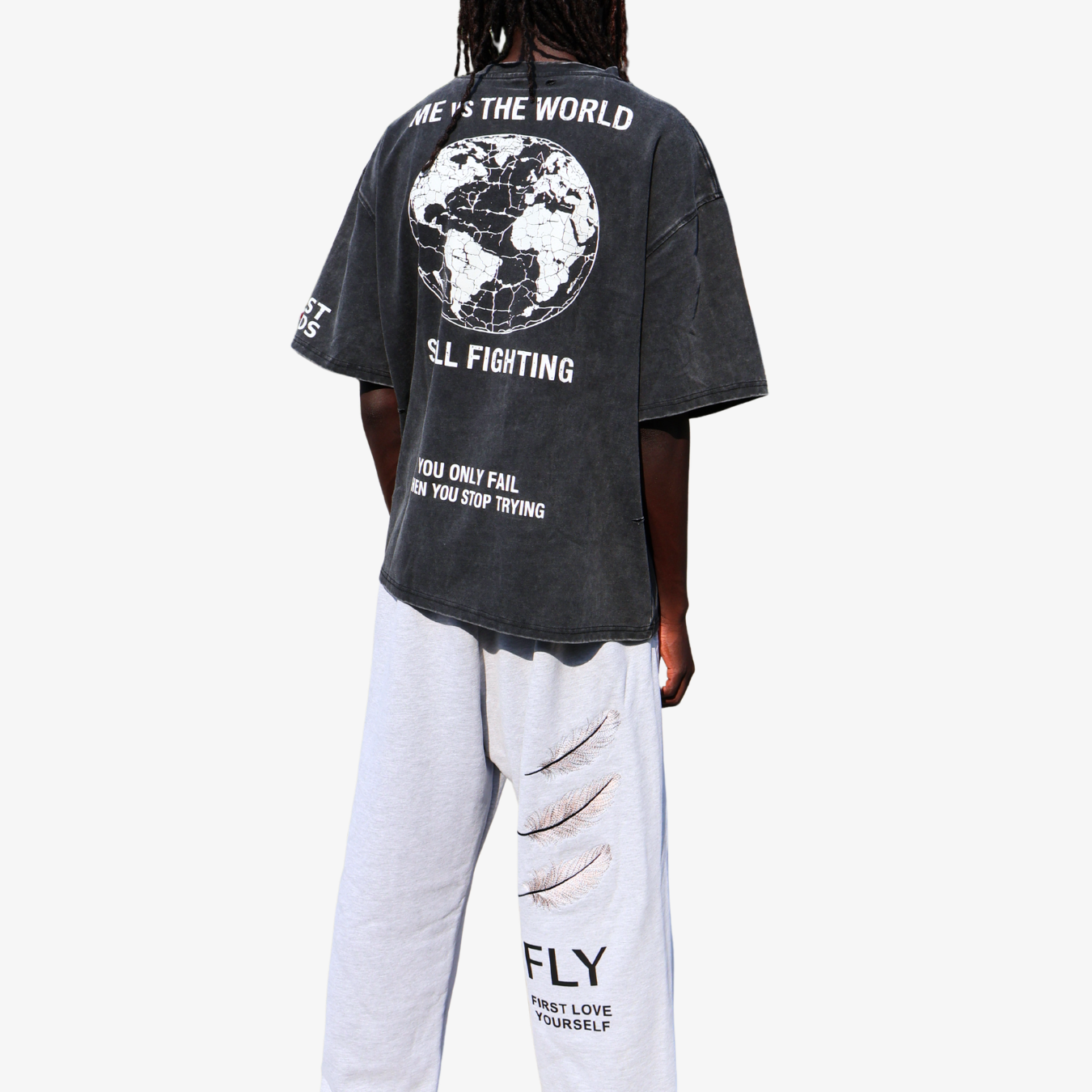 A person shown from the back wearing an oversized faded black graphic T-shirt with a large white globe print and text, paired with light gray distressed sweatpants, against a plain light gray background.